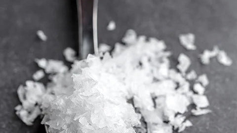 Spoonful of white salt on a dark surface